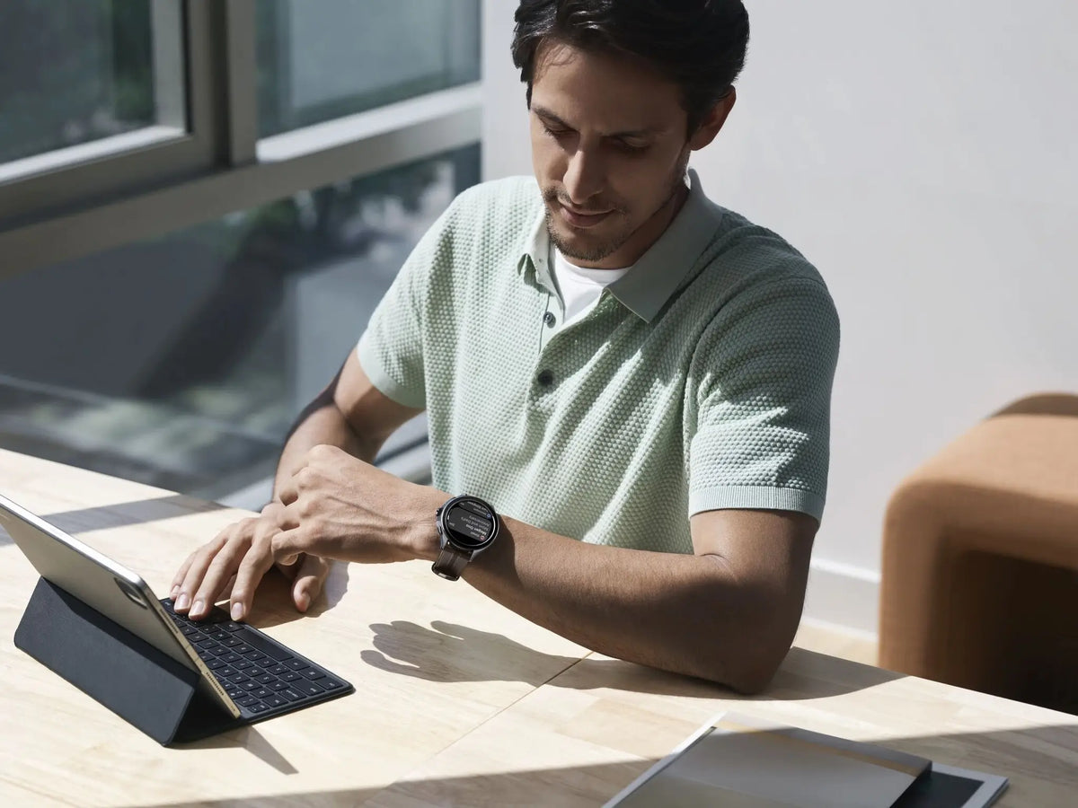 Man draagt Xiaomi Watch 2 Pro smartwatch terwijl hij aan het bureau aan een tablet werkt
