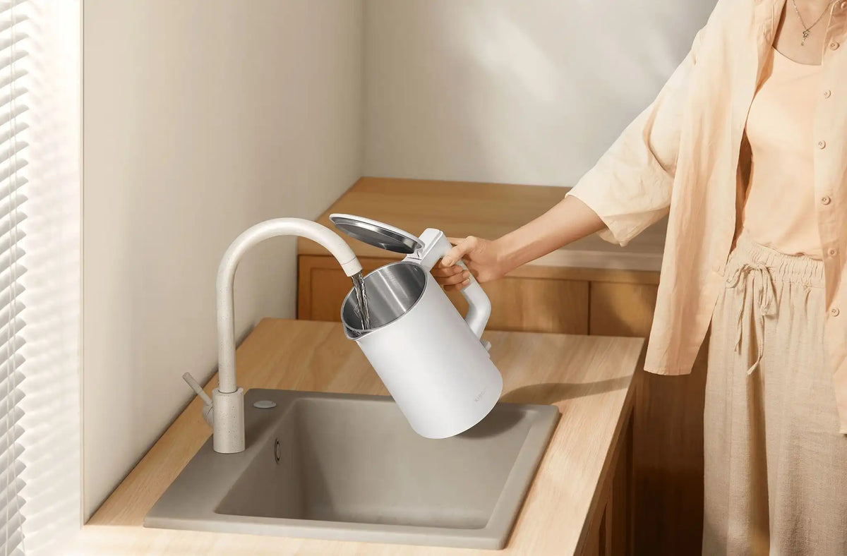 Vrouw schenkt water uit een witte Xiaomi waterkoker 2 Lite boven een aanrechtgootsteen