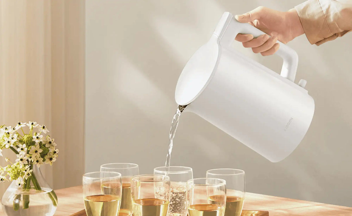 Persoon schenkt water uit een Xiaomi waterkoker in glazen op een tafel met bloemen