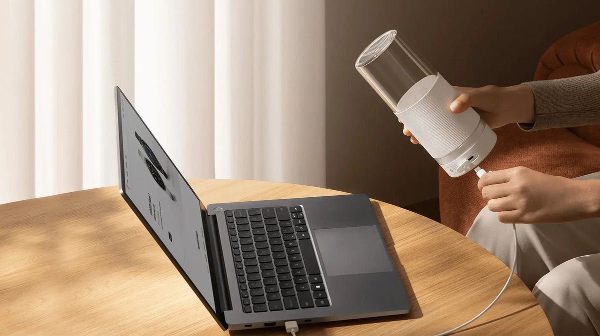 Persoon houdt een witte draagbare Xiaomi blender vast op het bureau bij een laptop